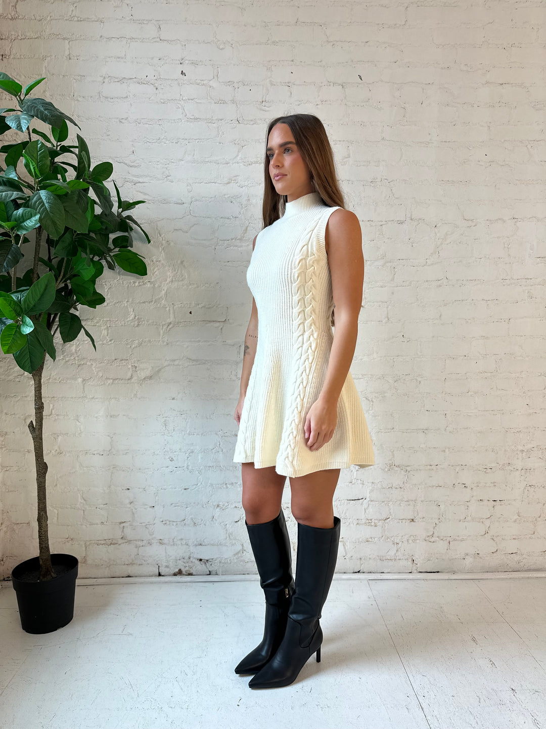 Woman wearing cream cable knit sweater mini dress with tall black knee boot. 