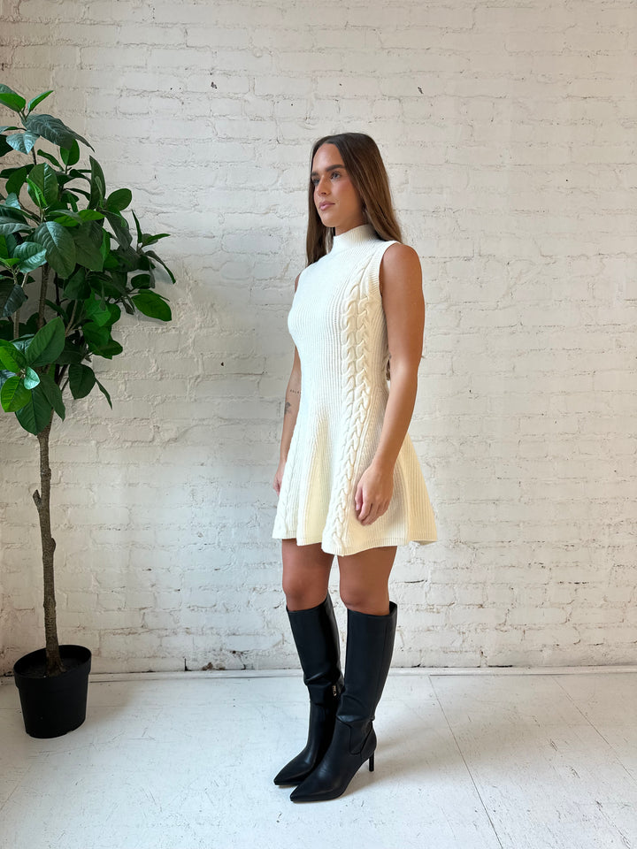 Woman wearing cream cable knit sweater mini dress with tall black knee boot. 