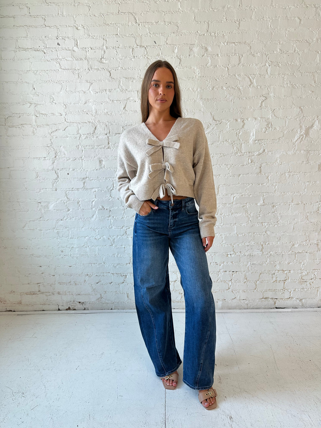 Woman wearing taupe knit reversible bow sweater with dark wash barrel jean.
