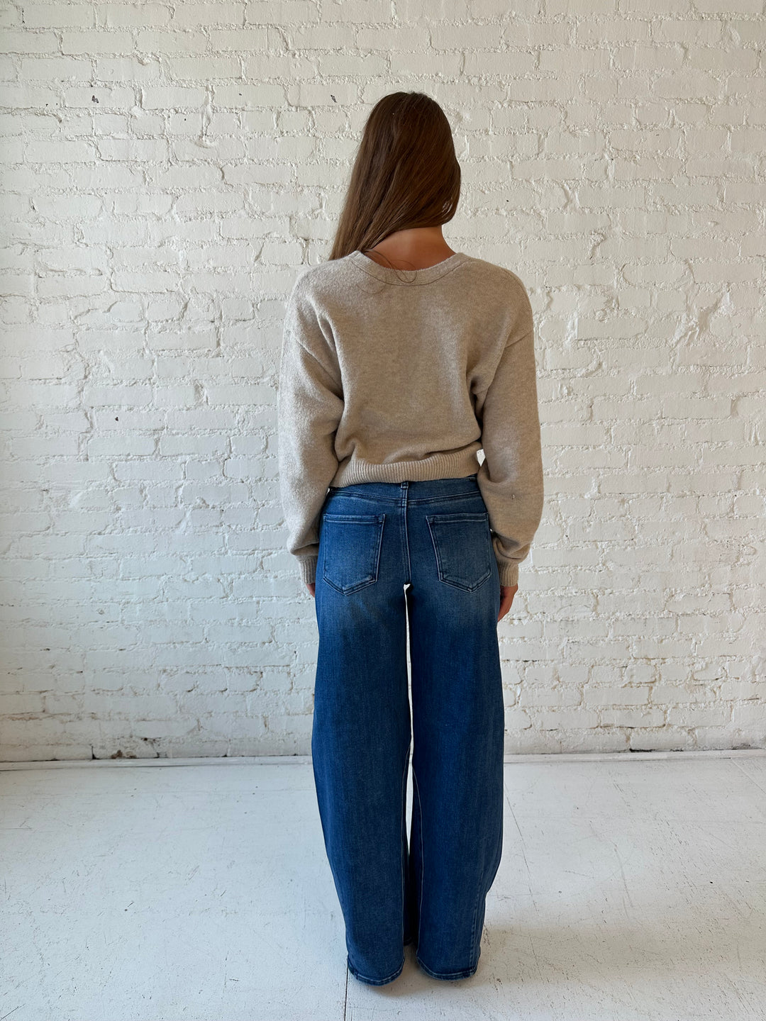 Woman wearing taupe knit reversible bow sweater with dark wash barrel jean.