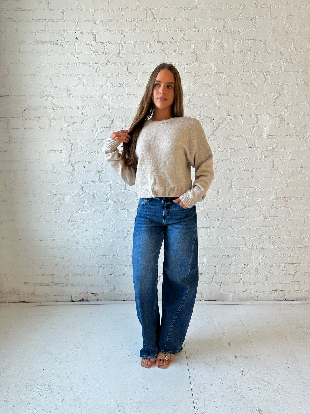 Woman wearing taupe knit reversible bow sweater with dark wash barrel jean.