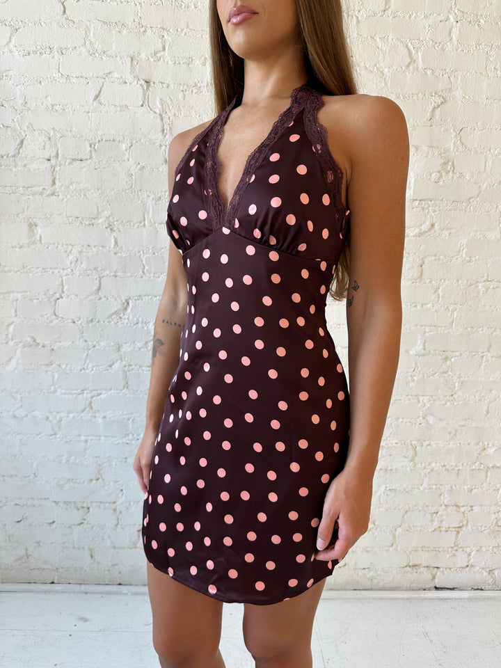Woman wearing burgundy polka dot mini dress with lace trim, self tie halter neckline, and open back.