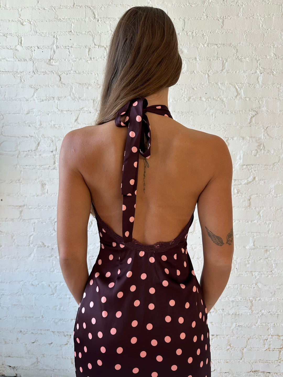 Woman wearing burgundy polka dot mini dress with lace trim, self tie halter neckline, and open back.