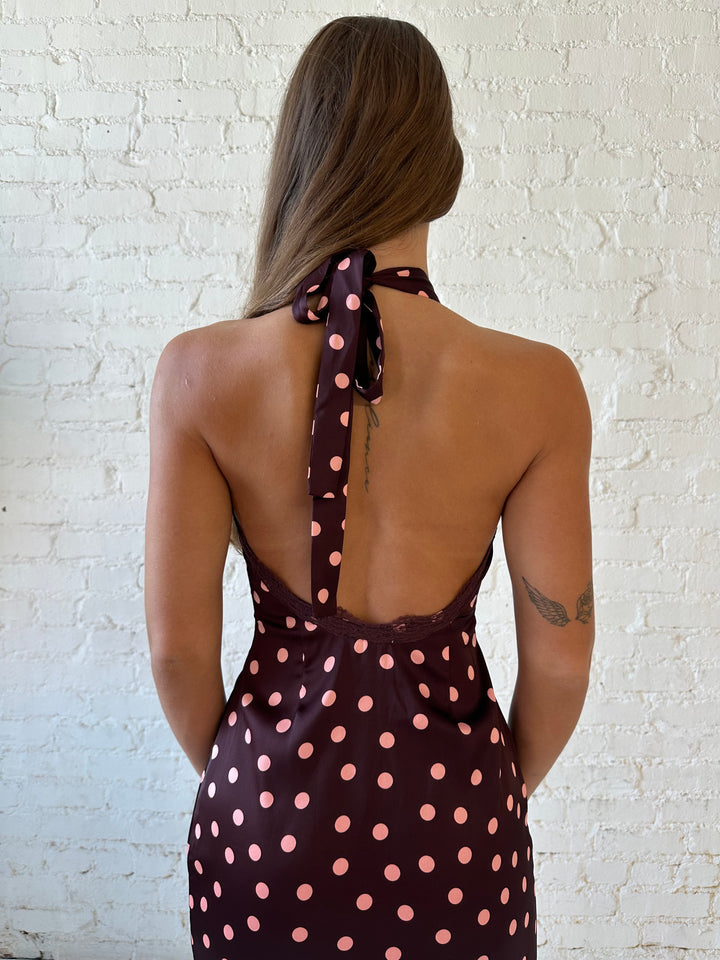 Woman wearing burgundy polka dot mini dress with lace trim, self tie halter neckline, and open back.