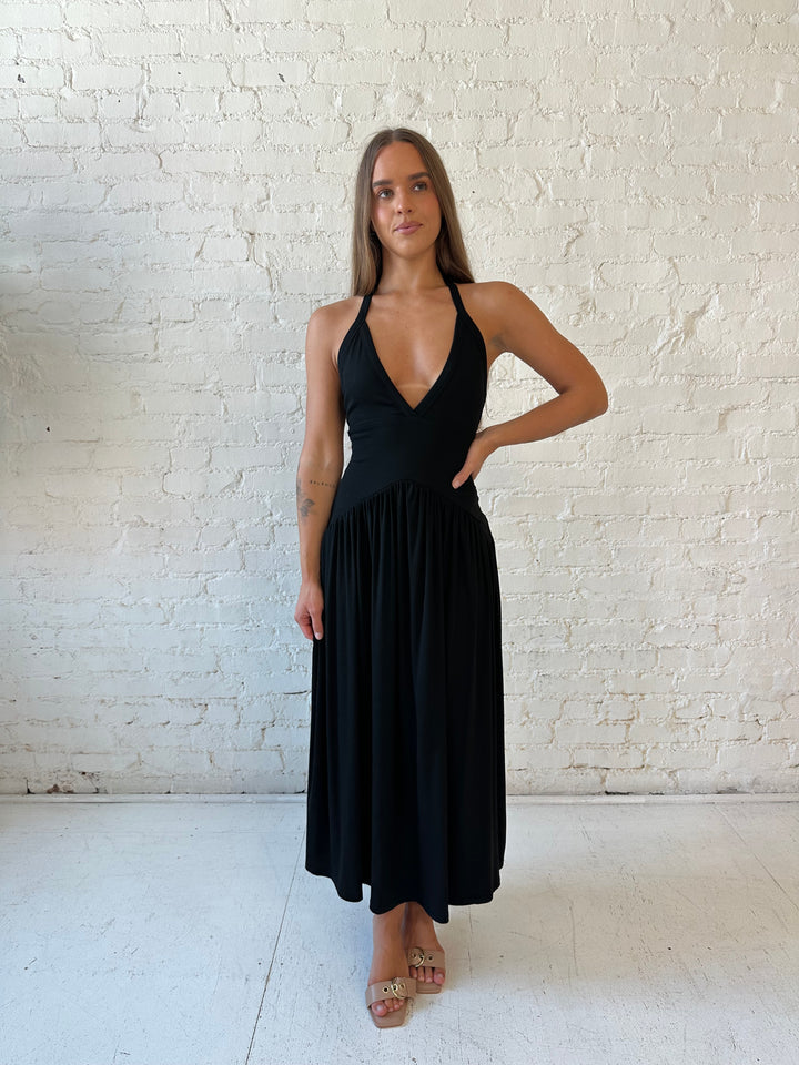 Woman wearing black maxi dress with plunging halter neckline and flowy skirt. 