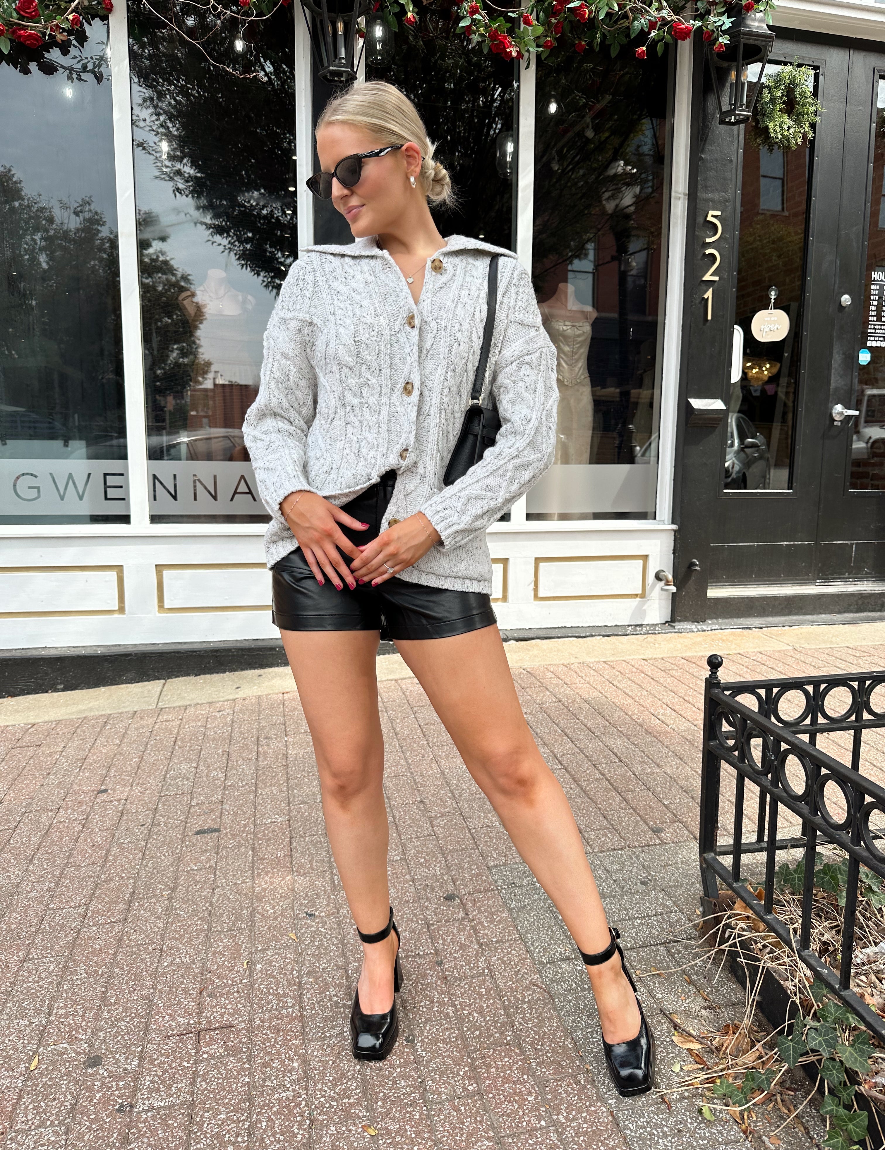 Woman wearing grey chinky oversized button down cardigan with black leather short.