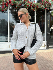 Woman wearing grey chinky oversized button down cardigan with black leather short.
