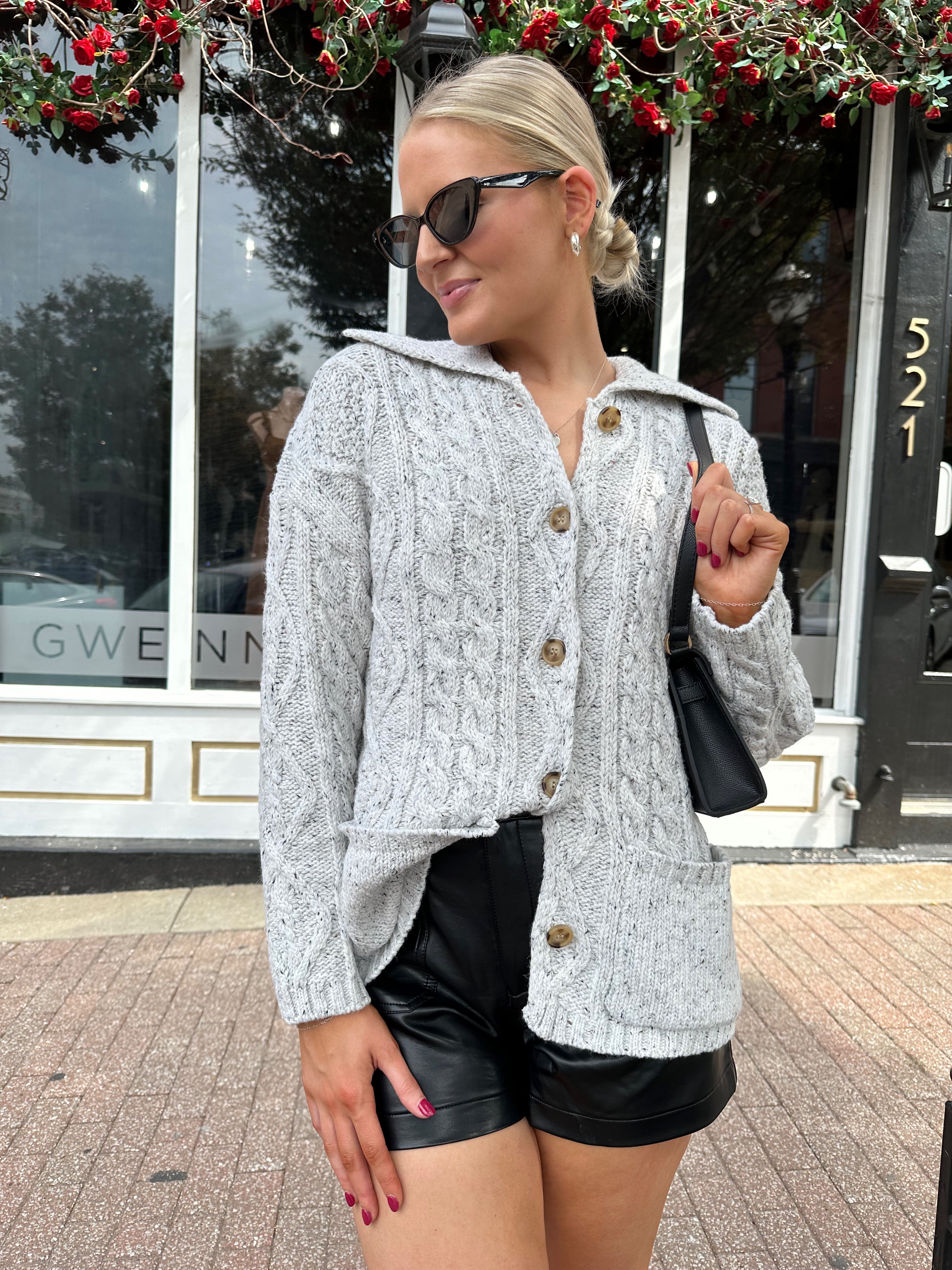 Woman wearing grey chinky oversized button down cardigan with black leather short.