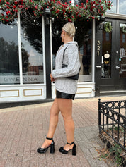 Woman wearing grey chinky oversized button down cardigan with black leather short.