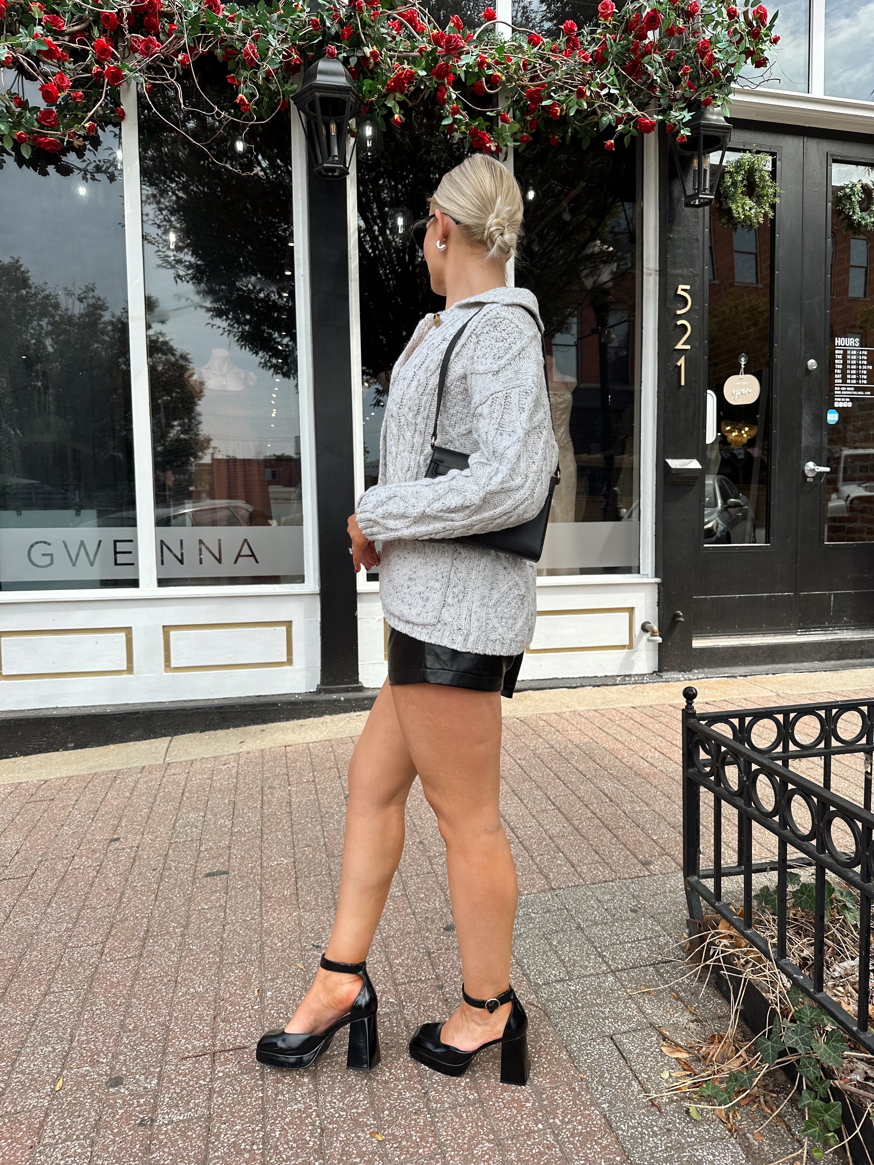 Woman wearing grey chinky oversized button down cardigan with black leather short.