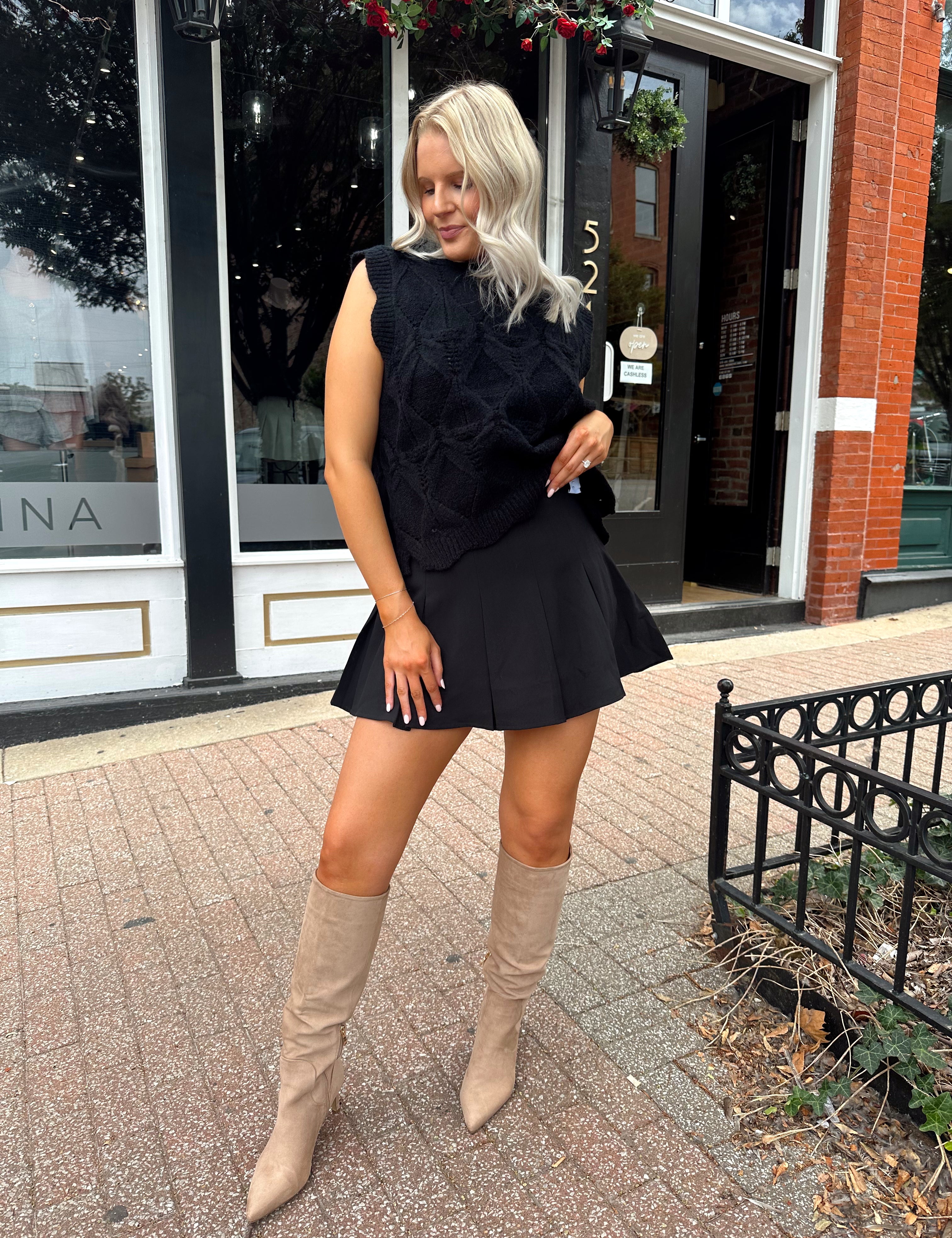 Woman wearing black sleeveless cable knit sweater with cream bow back.  