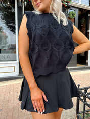 Woman wearing black sleeveless cable knit sweater with cream bow back.  