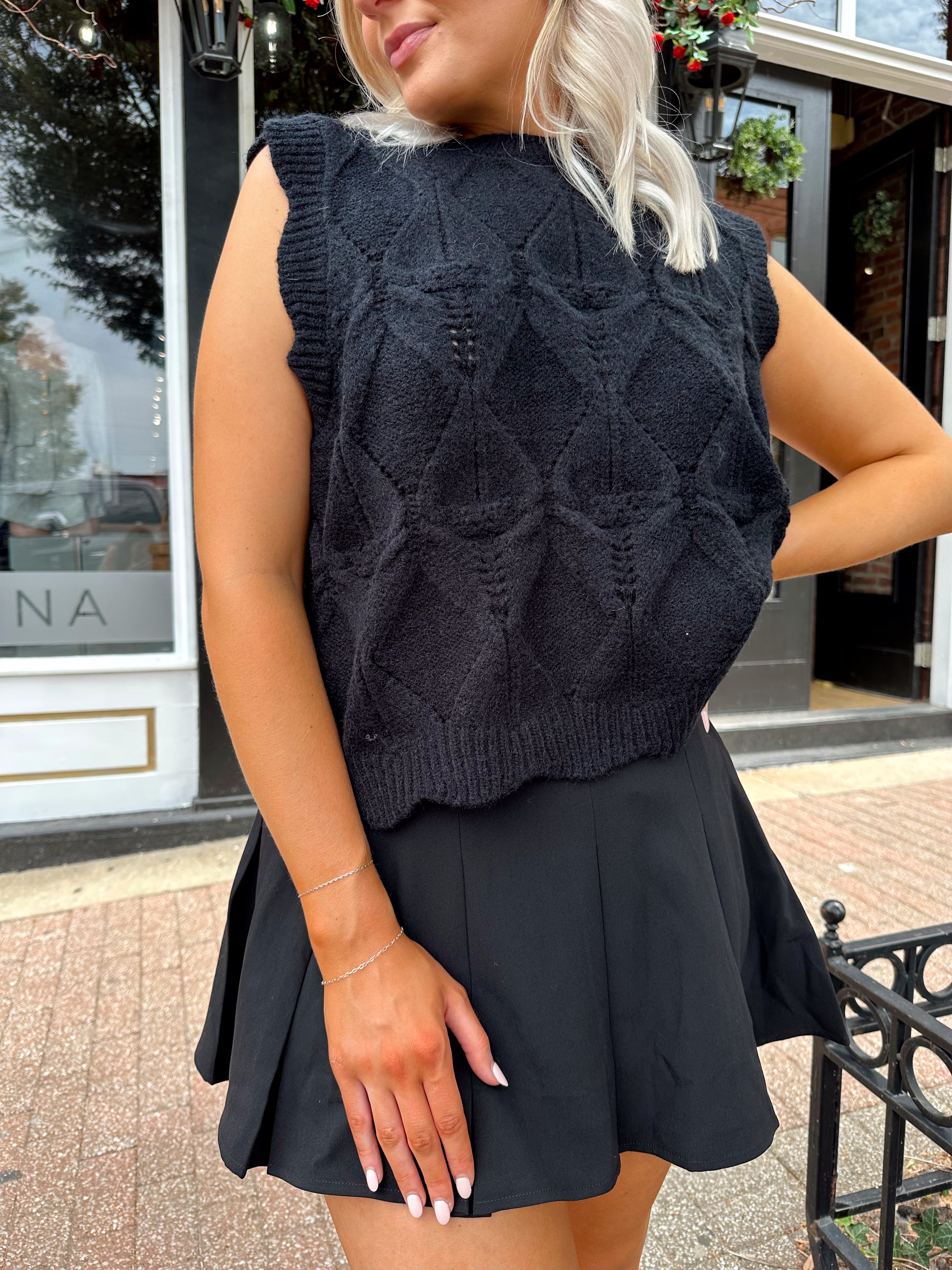 Woman wearing black sleeveless cable knit sweater with cream bow back.  