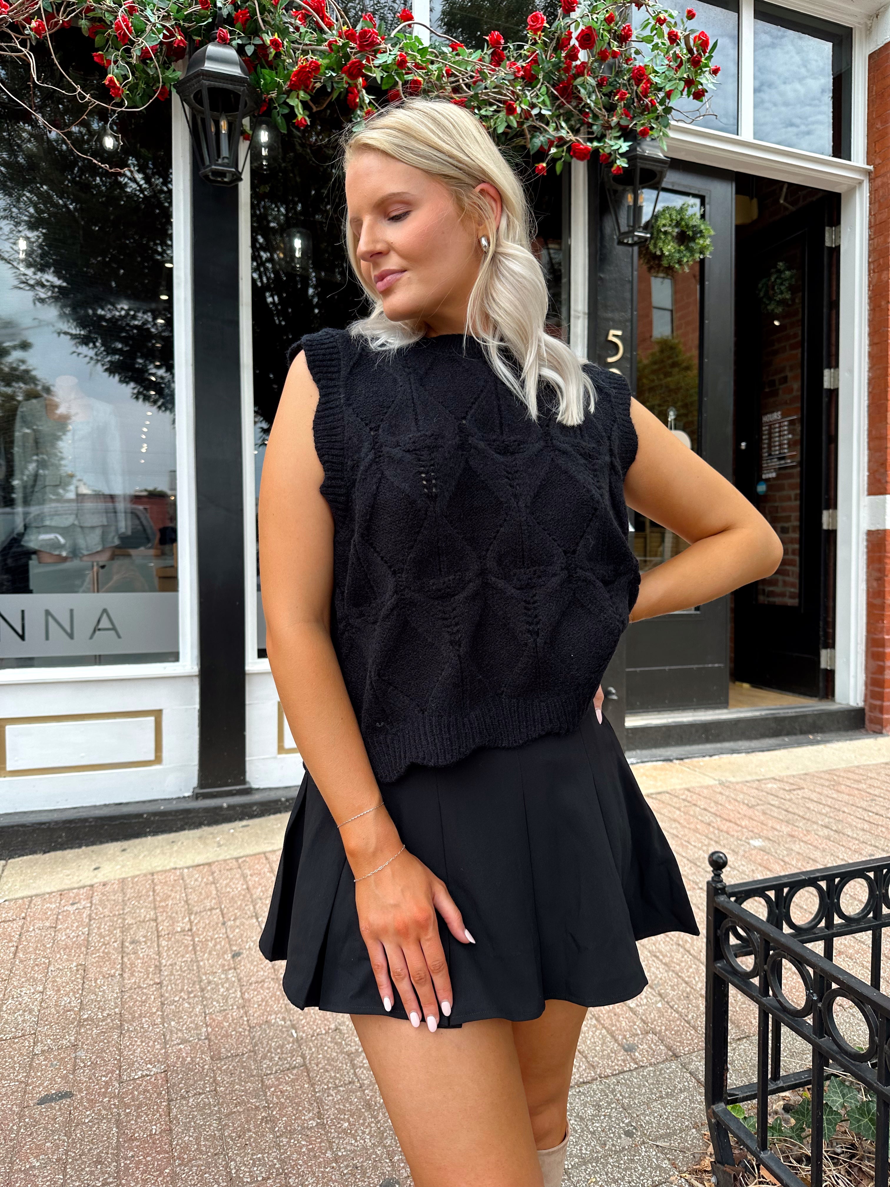 Woman wearing black sleeveless cable knit sweater with cream bow back.  