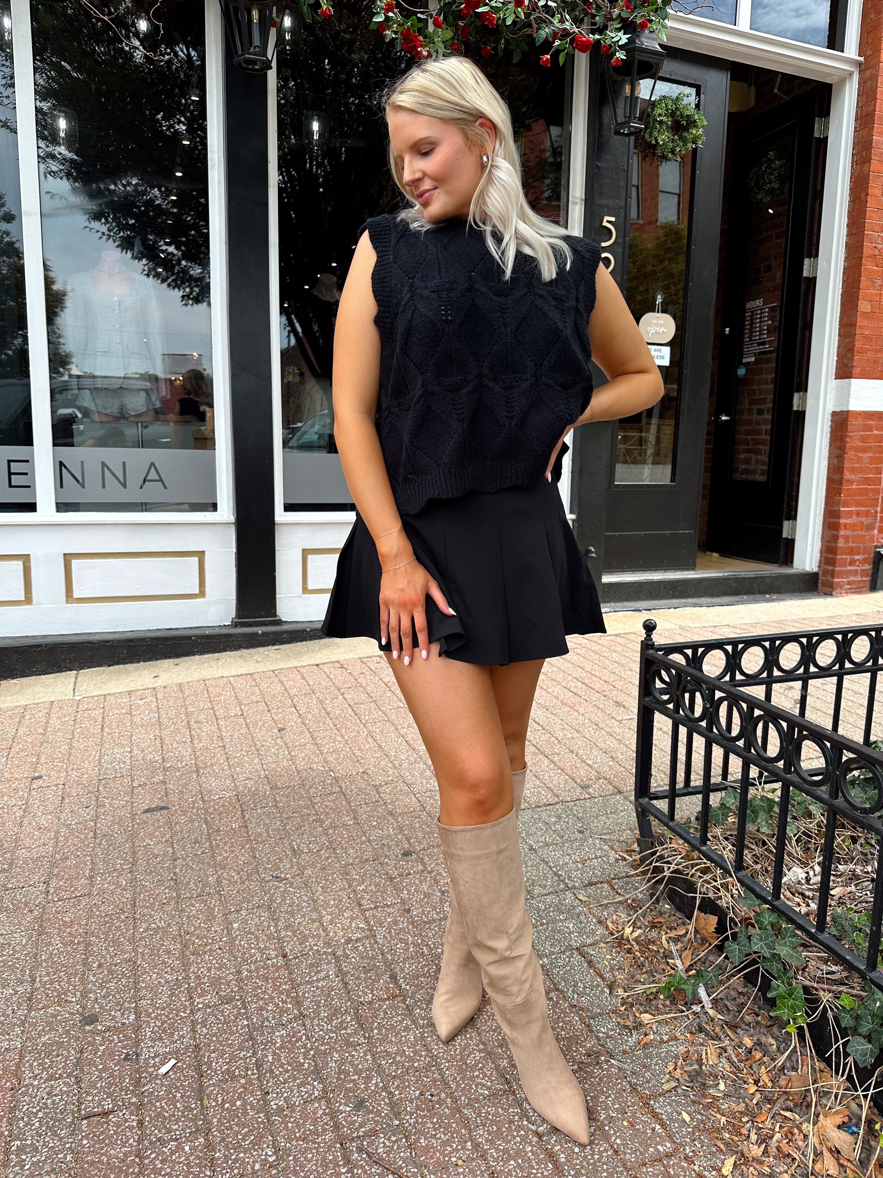 Woman wearing black sleeveless cable knit sweater with cream bow back.  