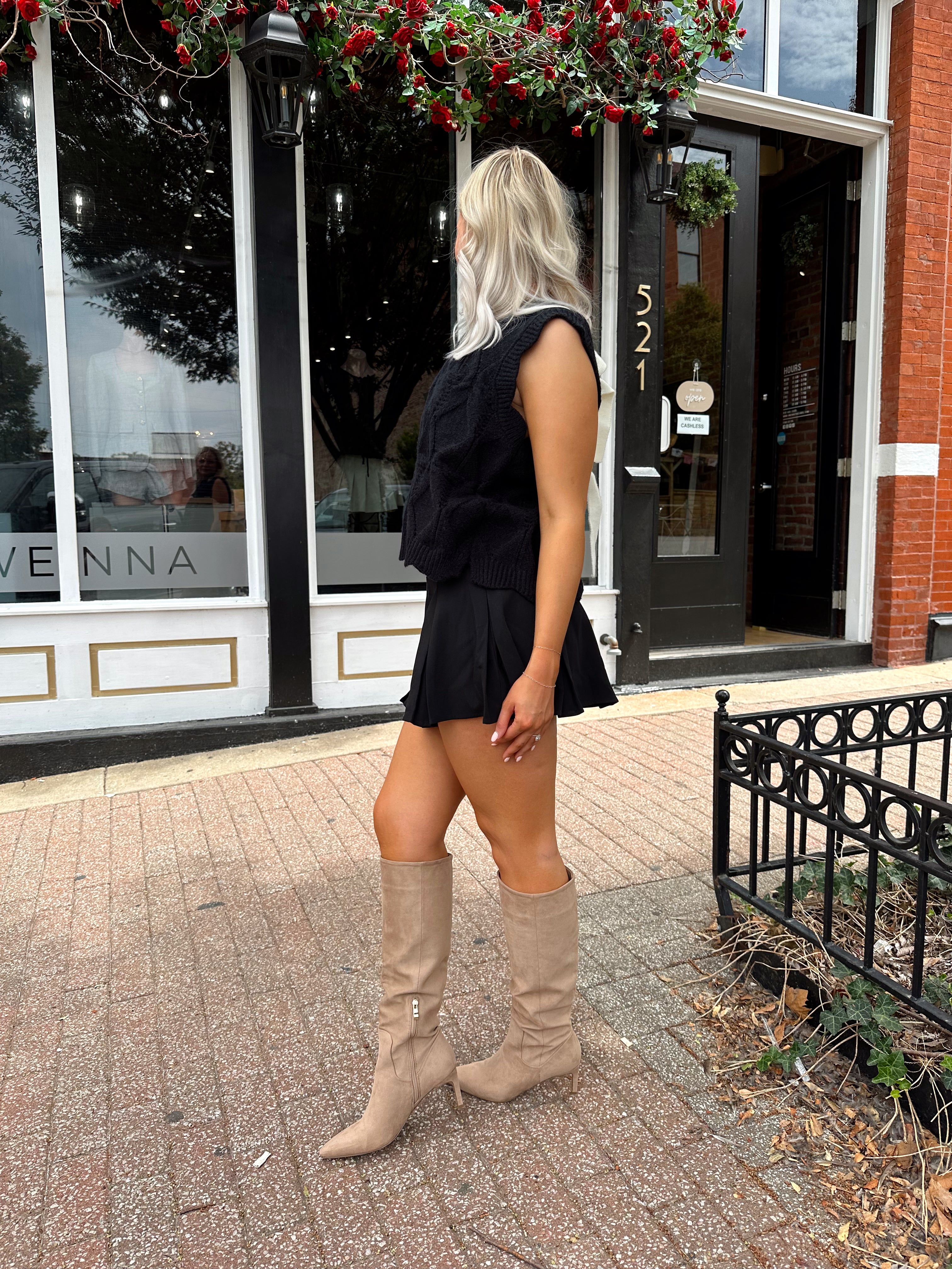 Woman wearing black sleeveless cable knit sweater with cream bow back.  