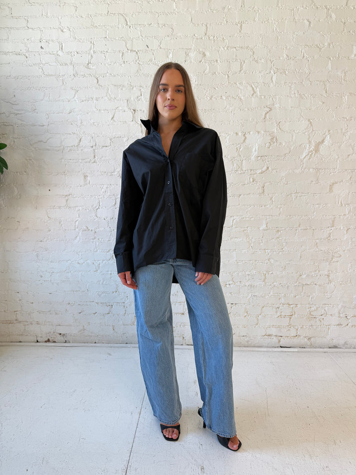 Woman wearing black oversized button down top with medium wash jeans. 