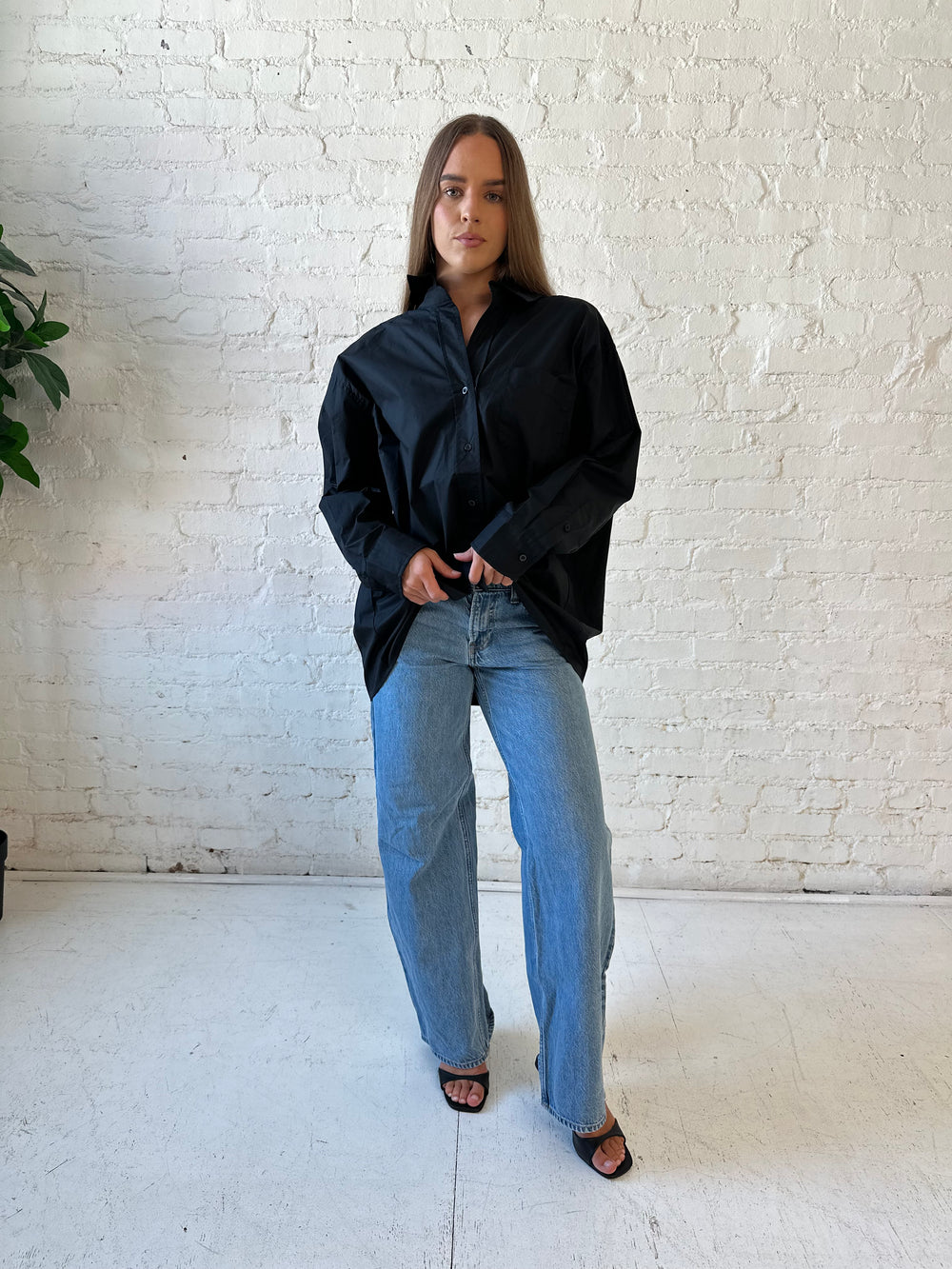 Woman wearing black oversized button down top with medium wash jeans. 