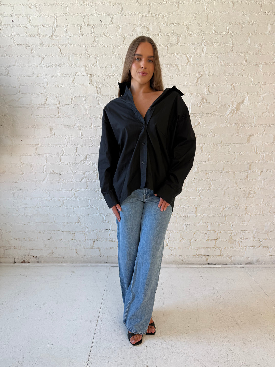 Woman wearing black oversized button down top with medium wash jeans. 