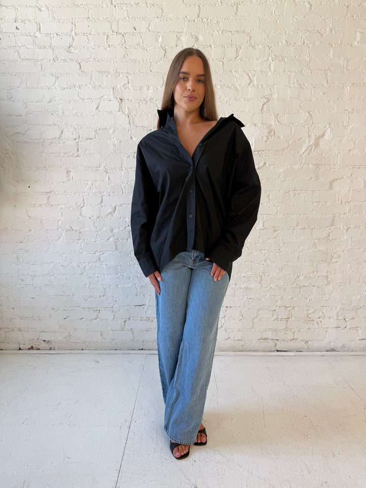 Woman wearing black oversized button down top with medium wash jeans. 