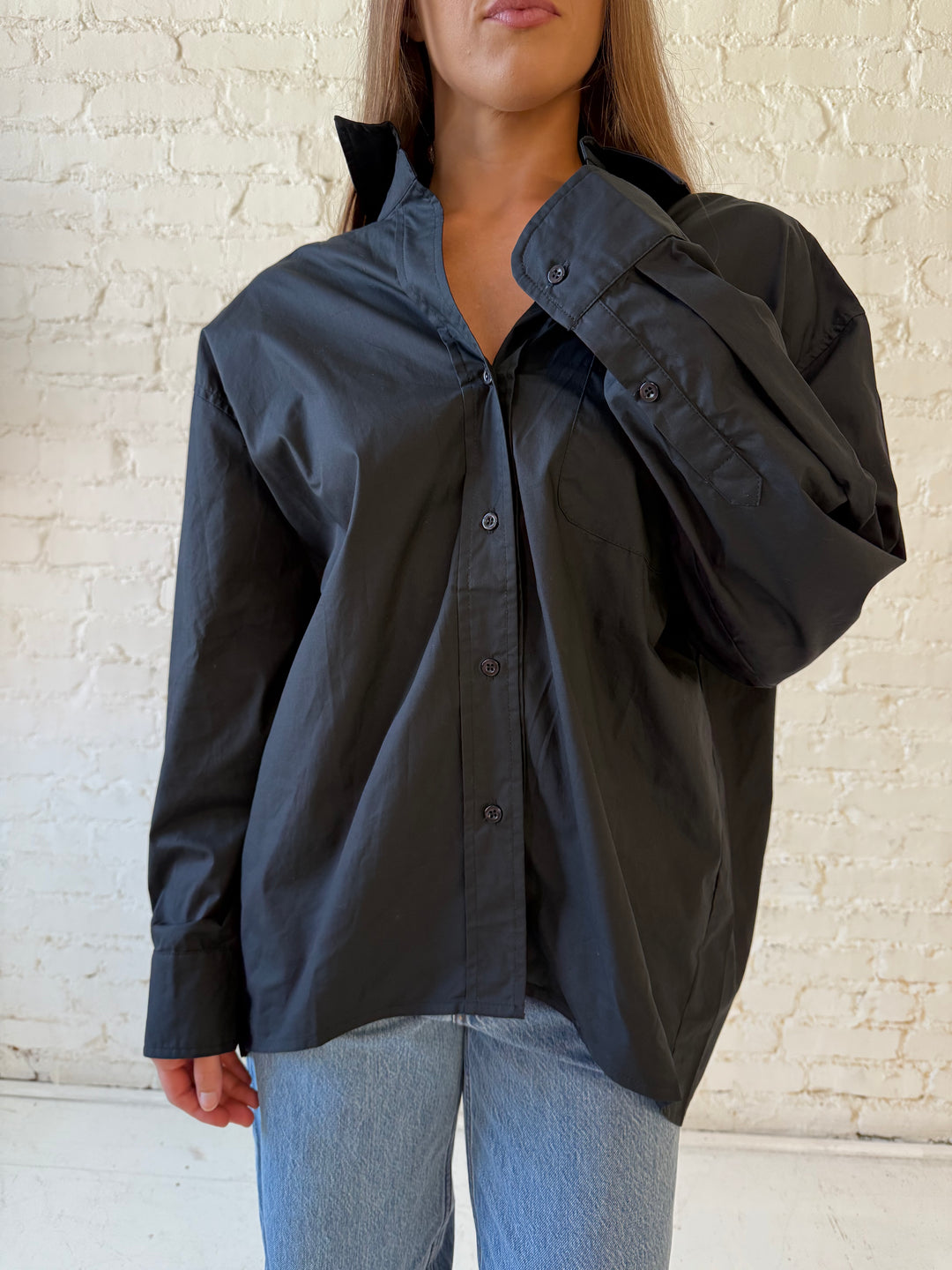 Woman wearing black oversized button down top with medium wash jeans. 