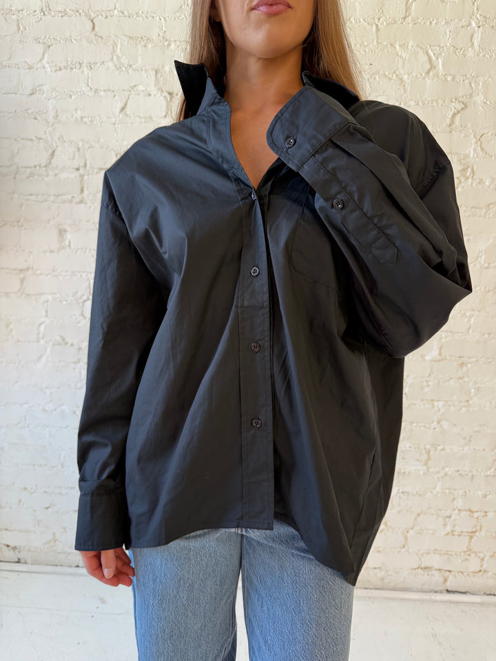Woman wearing black oversized button down top with medium wash jeans. 