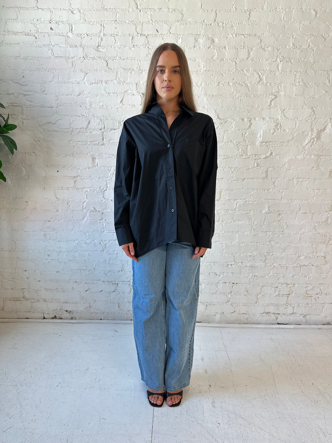 Woman wearing black oversized button down top with medium wash jeans. 