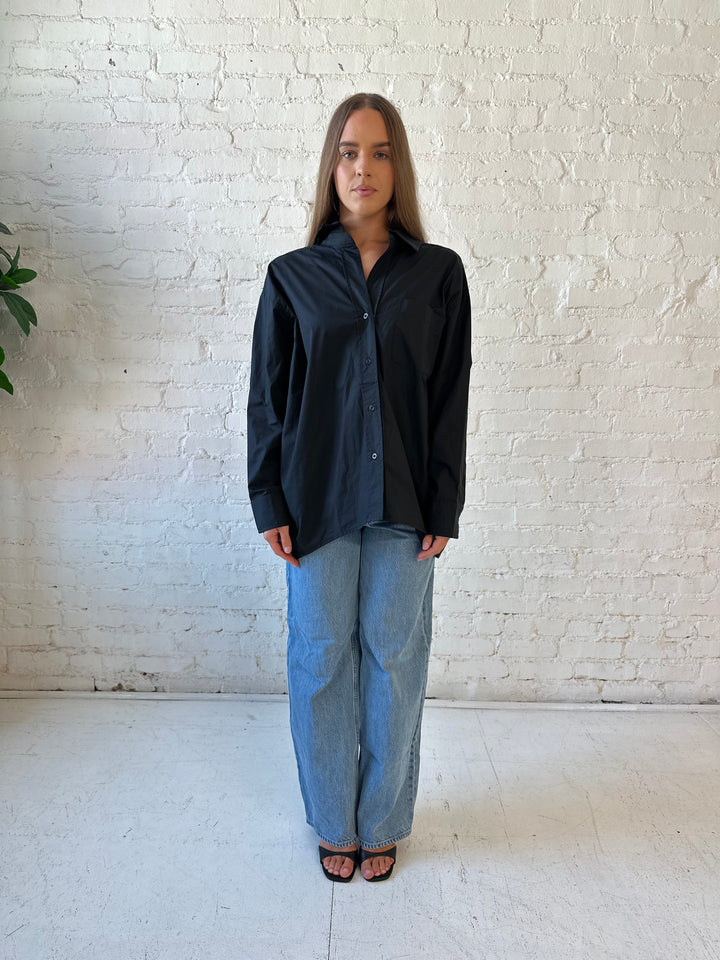 Woman wearing black oversized button down top with medium wash jeans. 