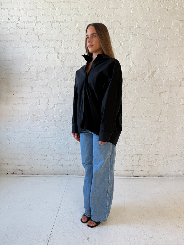 Woman wearing black oversized button down top with medium wash jeans. 