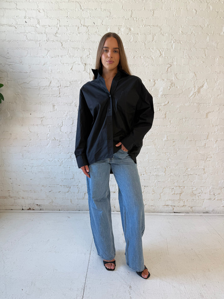 Woman wearing black oversized button down top with medium wash jeans. 