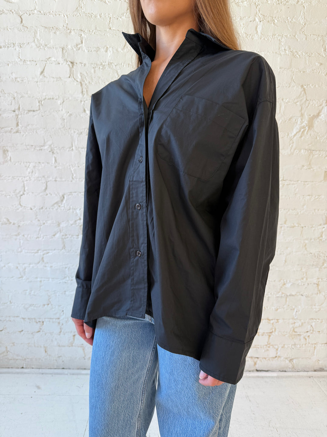 Woman wearing black oversized button down top with medium wash jeans. 