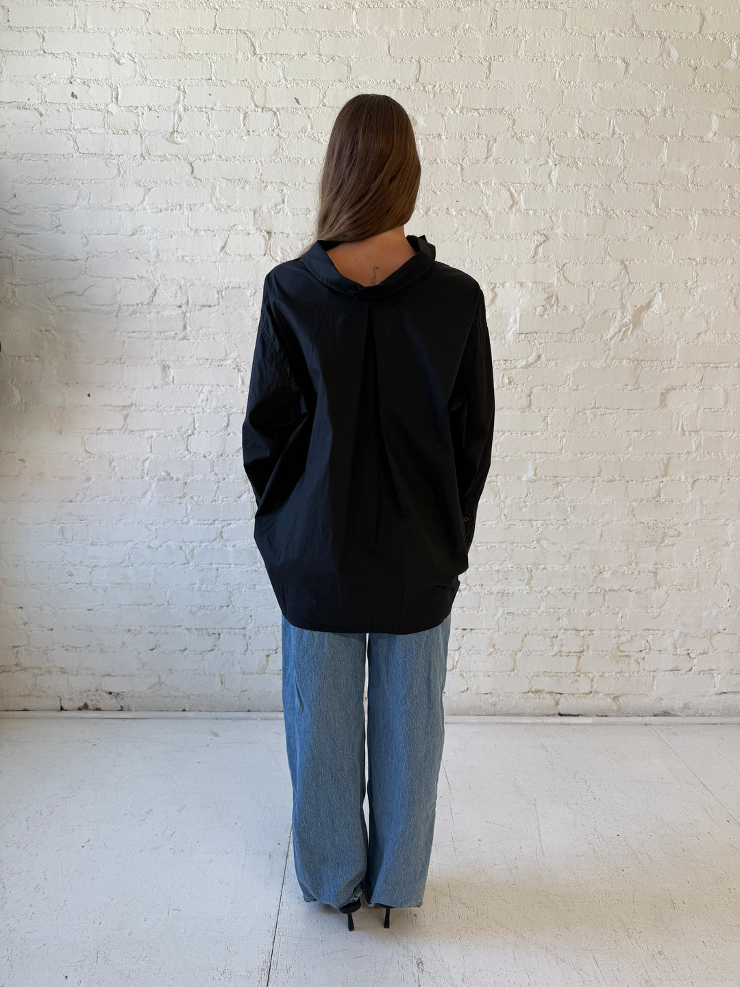 Woman wearing black oversized button down top with medium wash jeans. 