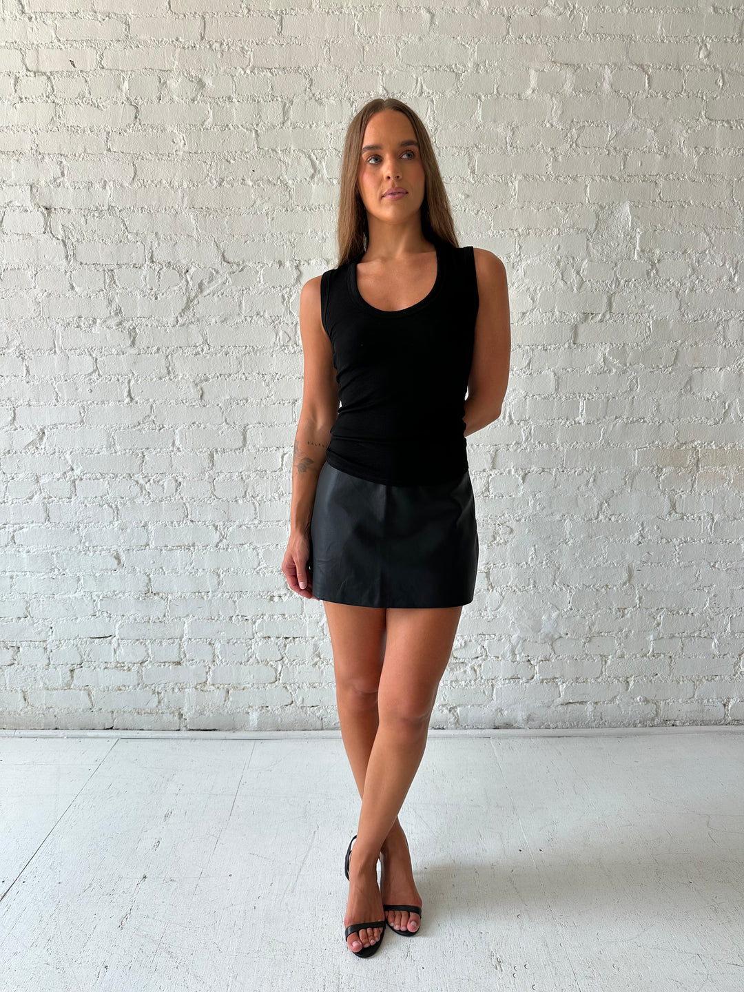 Woman wearing black scoop neck tank top with black leather mini skort. 