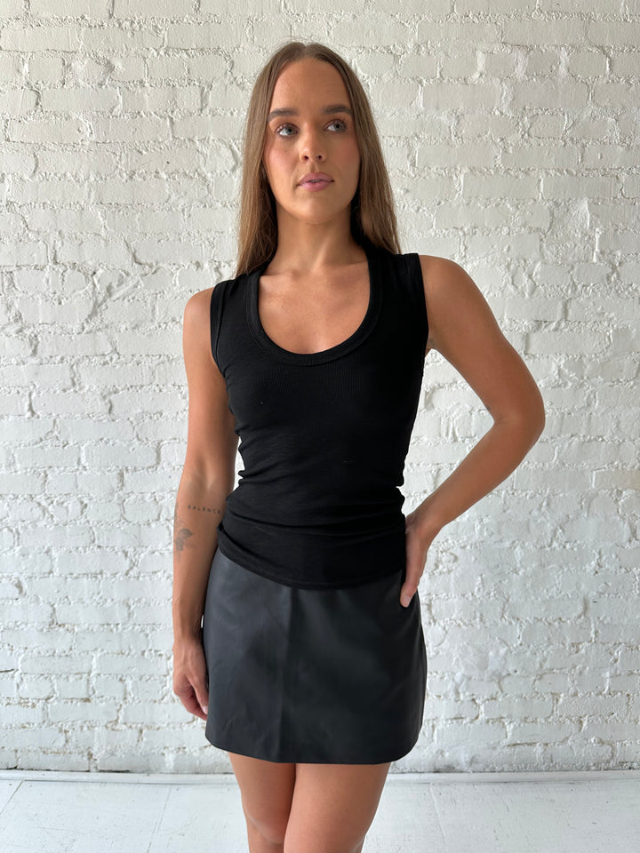 Woman wearing black scoop neck tank top with black leather mini skort. 