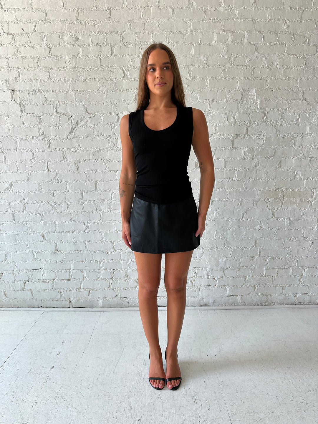 Woman wearing black scoop neck tank top with black leather mini skort. 