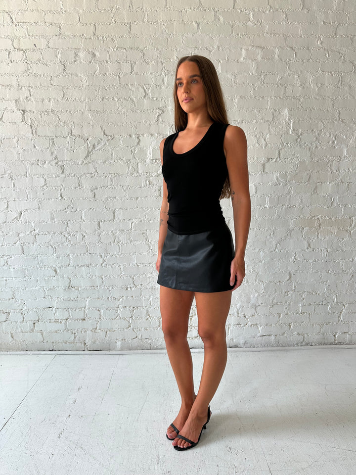 Woman wearing black scoop neck tank top with black leather mini skort. 