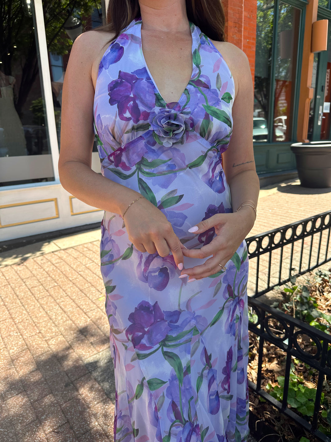 Woman wearing purple floral halter maxi dress with rosette detail. 