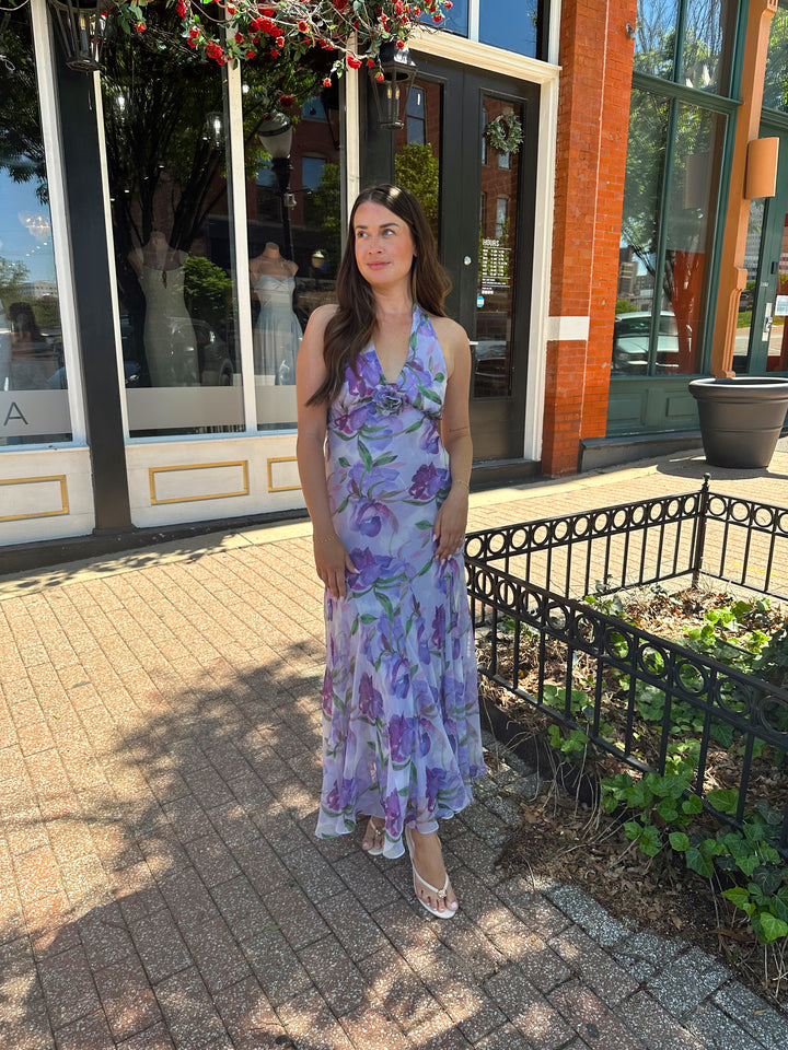 Woman wearing purple floral halter maxi dress with rosette detail. 