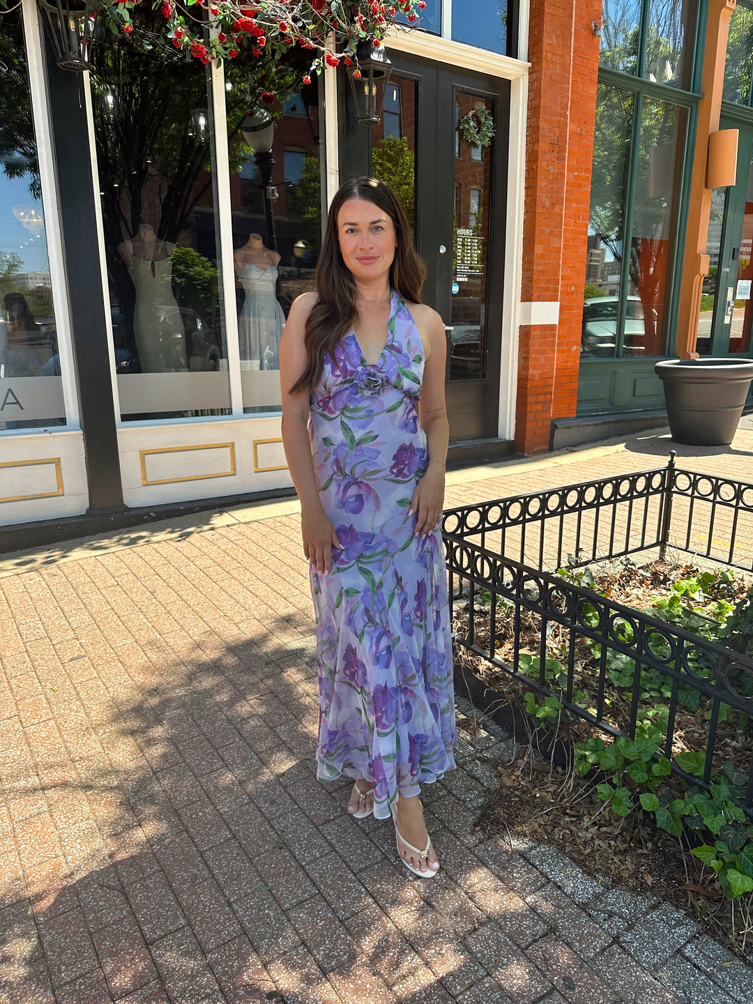 Woman wearing purple floral halter maxi dress with rosette detail. 