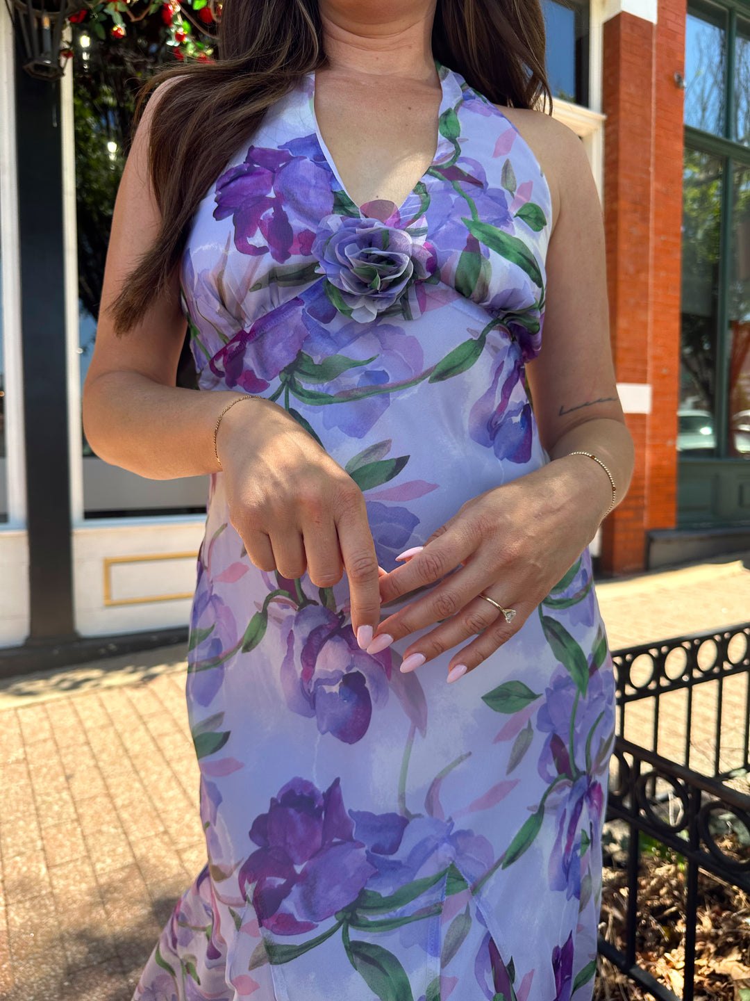 Woman wearing purple floral halter maxi dress with rosette detail. 