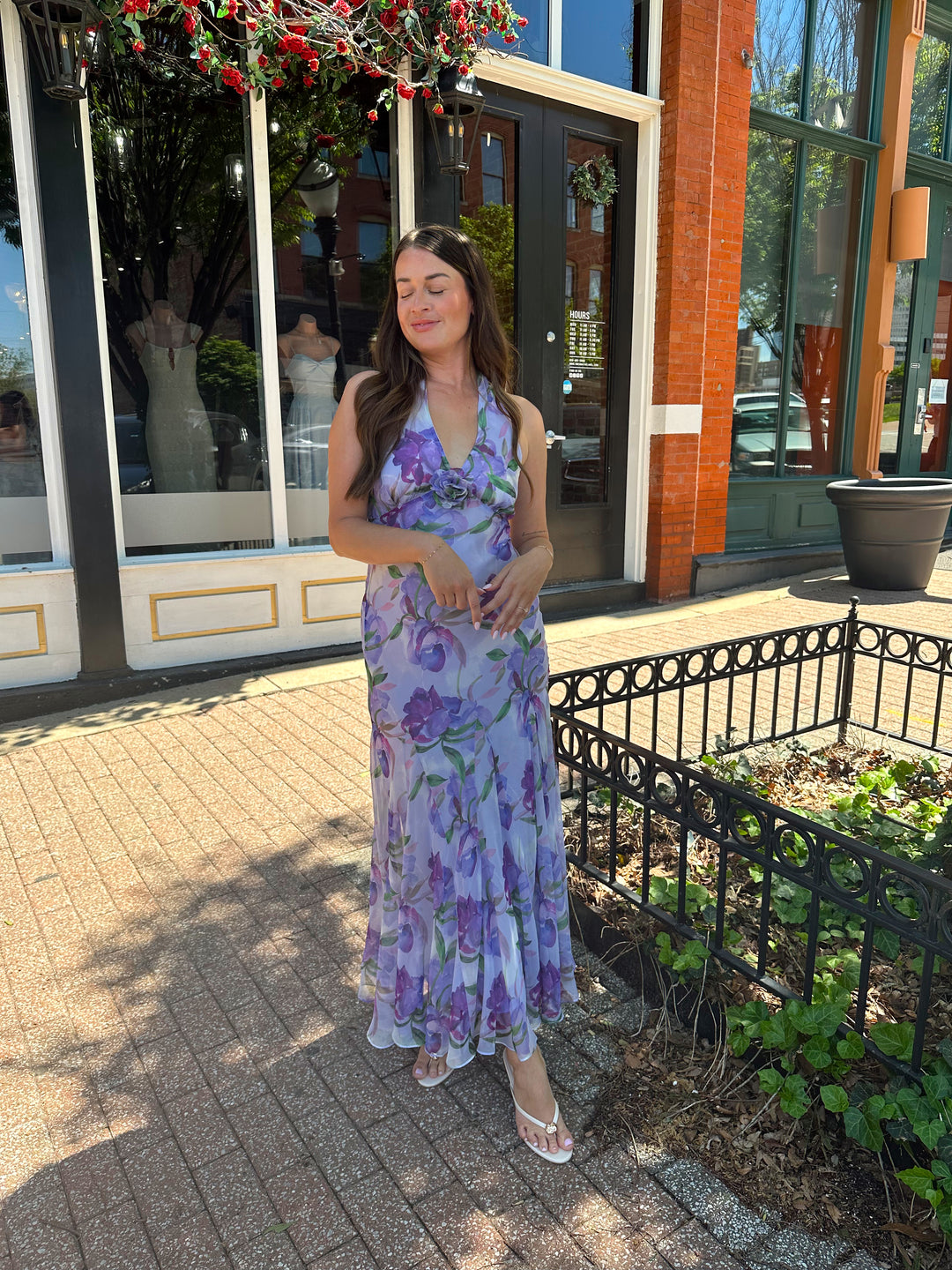 Woman wearing purple floral halter maxi dress with rosette detail. 