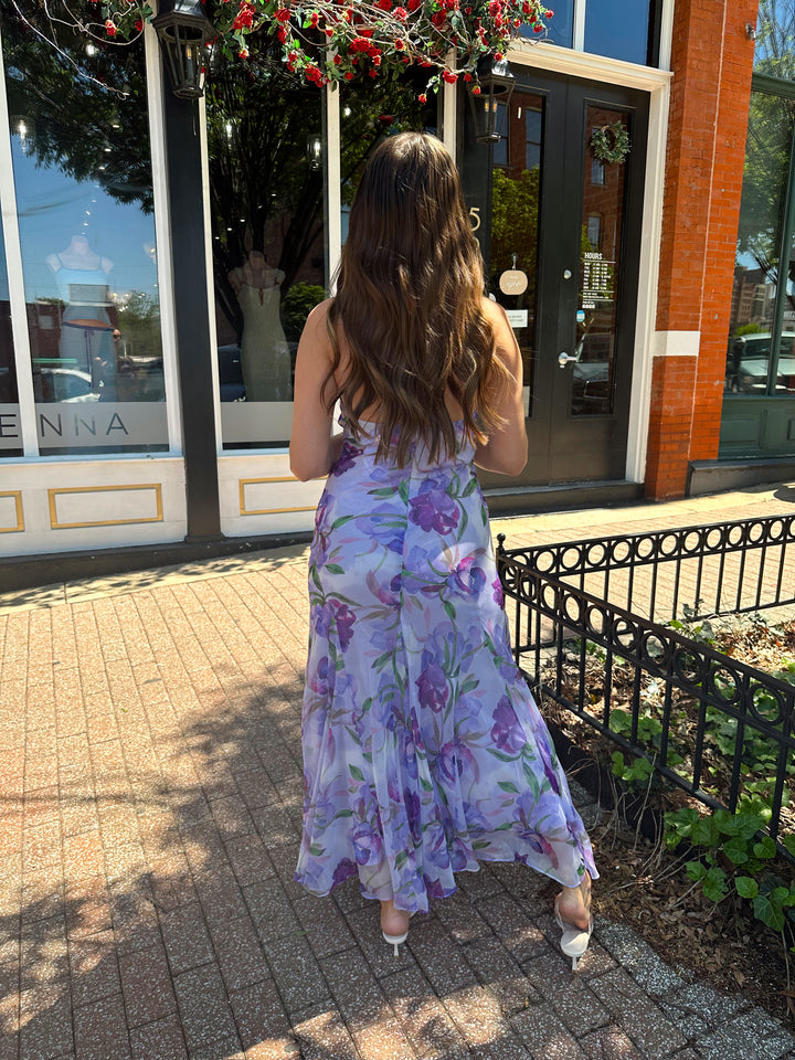 Woman wearing purple floral halter maxi dress with rosette detail. 