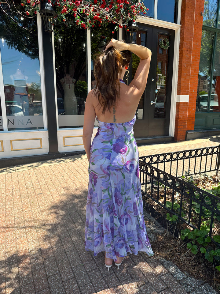 Woman wearing purple floral halter maxi dress with rosette detail. 