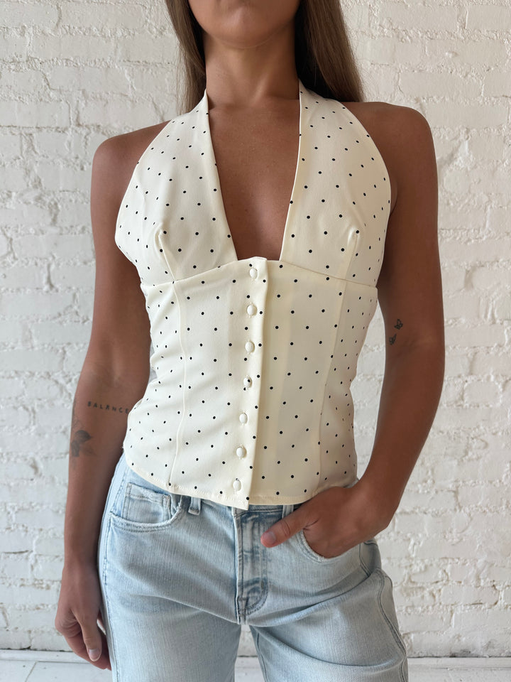 Woman wearing white and black polka dot halter top with light wash barrel jean.