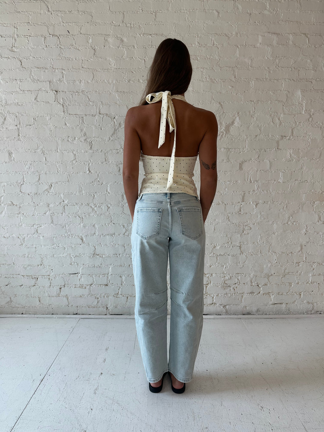 Woman wearing white and black polka dot halter top with light wash barrel jean.