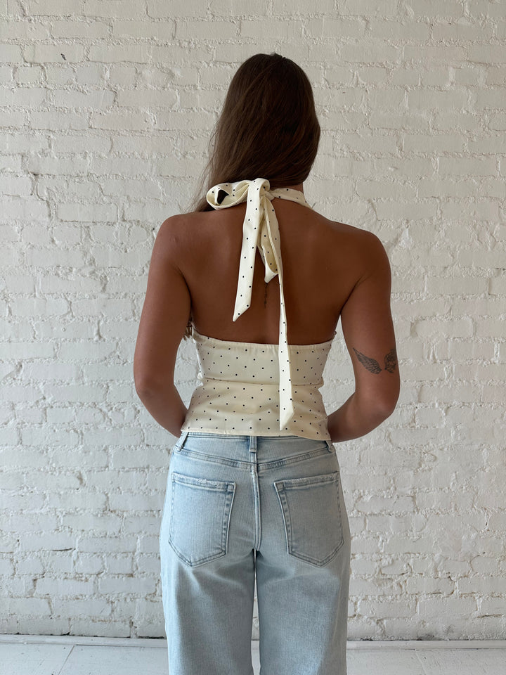 Woman wearing white and black polka dot halter top with light wash barrel jean.