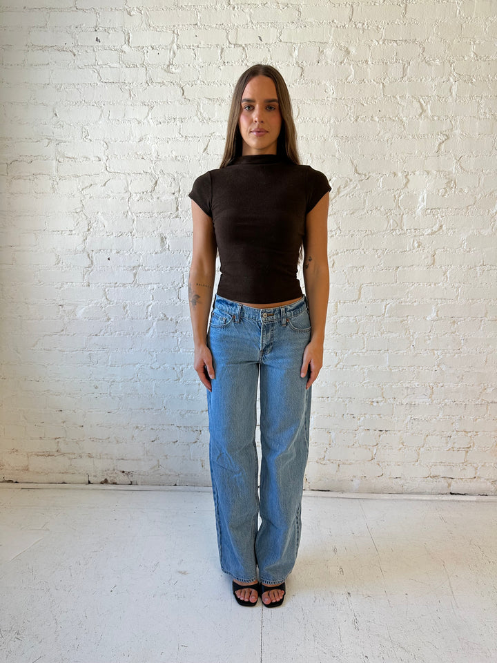 Woman wearing dark brown mock neck fitted top with medium wash jean and heel.