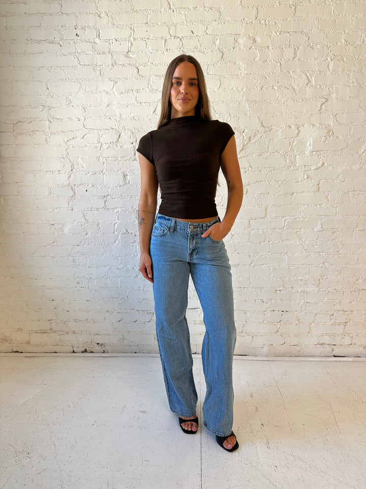 Woman wearing dark brown mock neck fitted top with medium wash jean and heel.