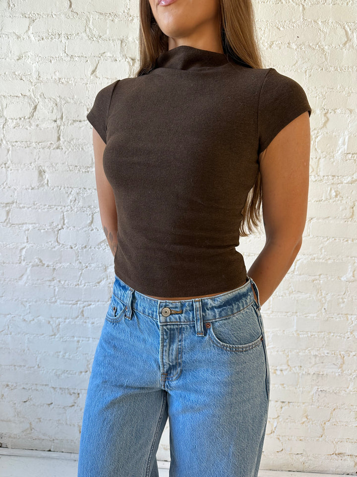 Woman wearing dark brown mock neck fitted top with medium wash jean and heel.