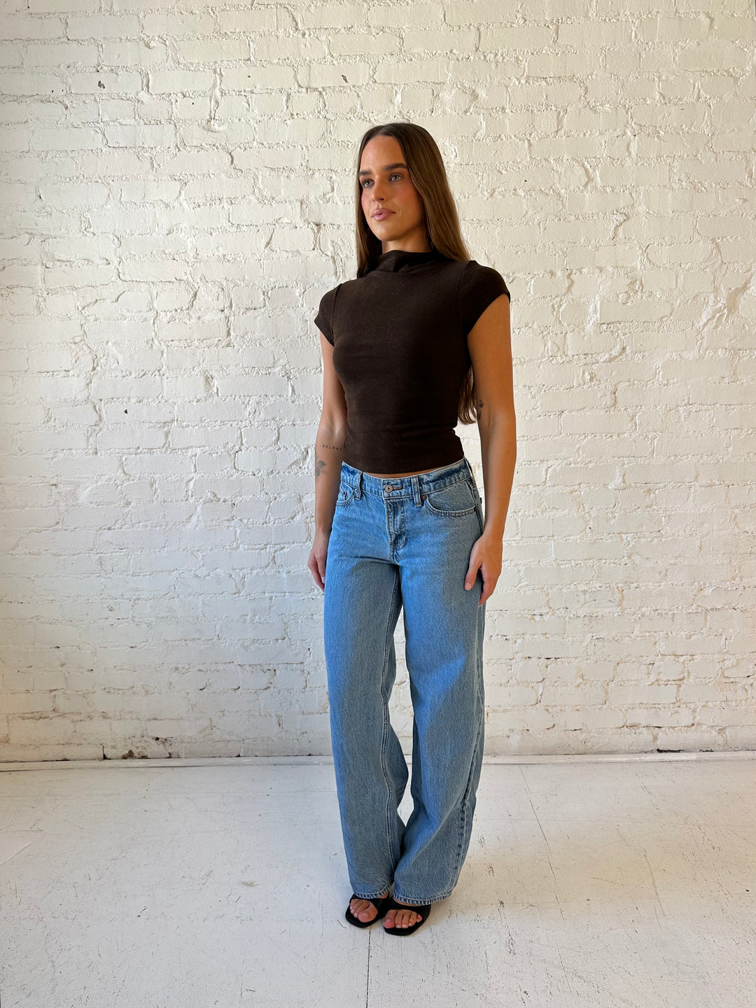 Woman wearing dark brown mock neck fitted top with medium wash jean and heel.